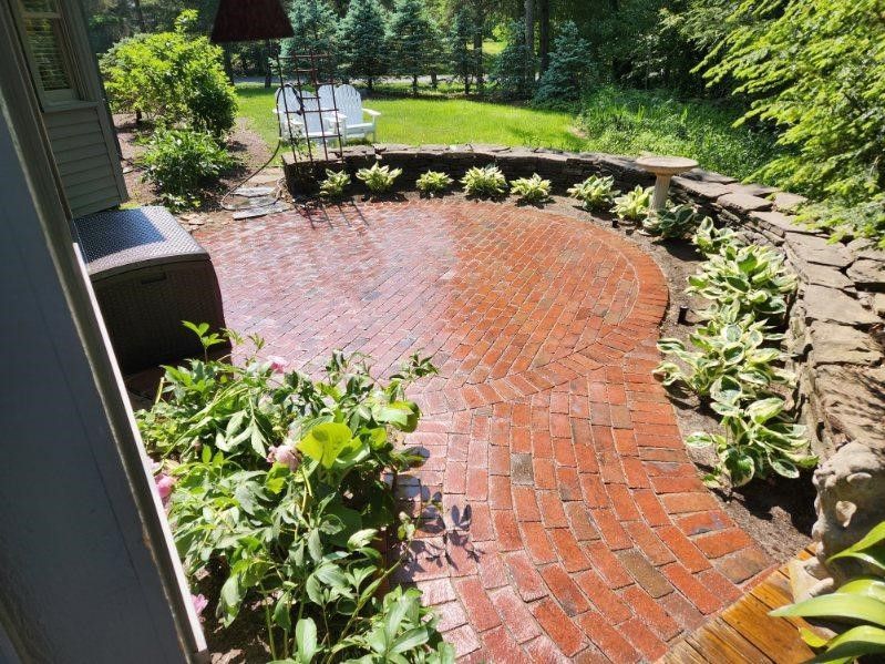 A brick patio with a stone wall and chairs in a backyard.