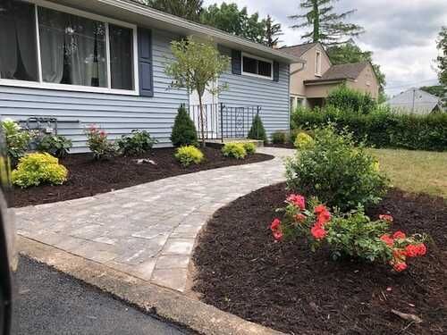 Pathway leading to a light blue house with a landscaped yard and various plants.