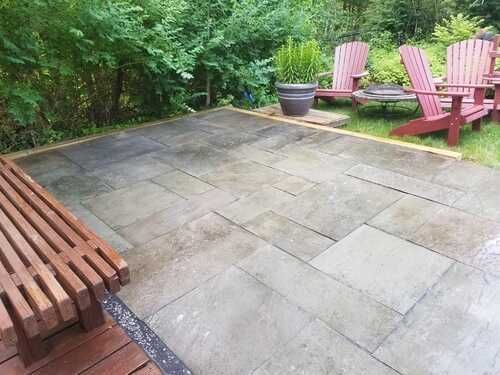 Patio with flagstone pavers, wooden bench, red Adirondack chairs, and greenery.