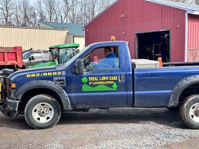 A blue truck is parked in front of a red barn.