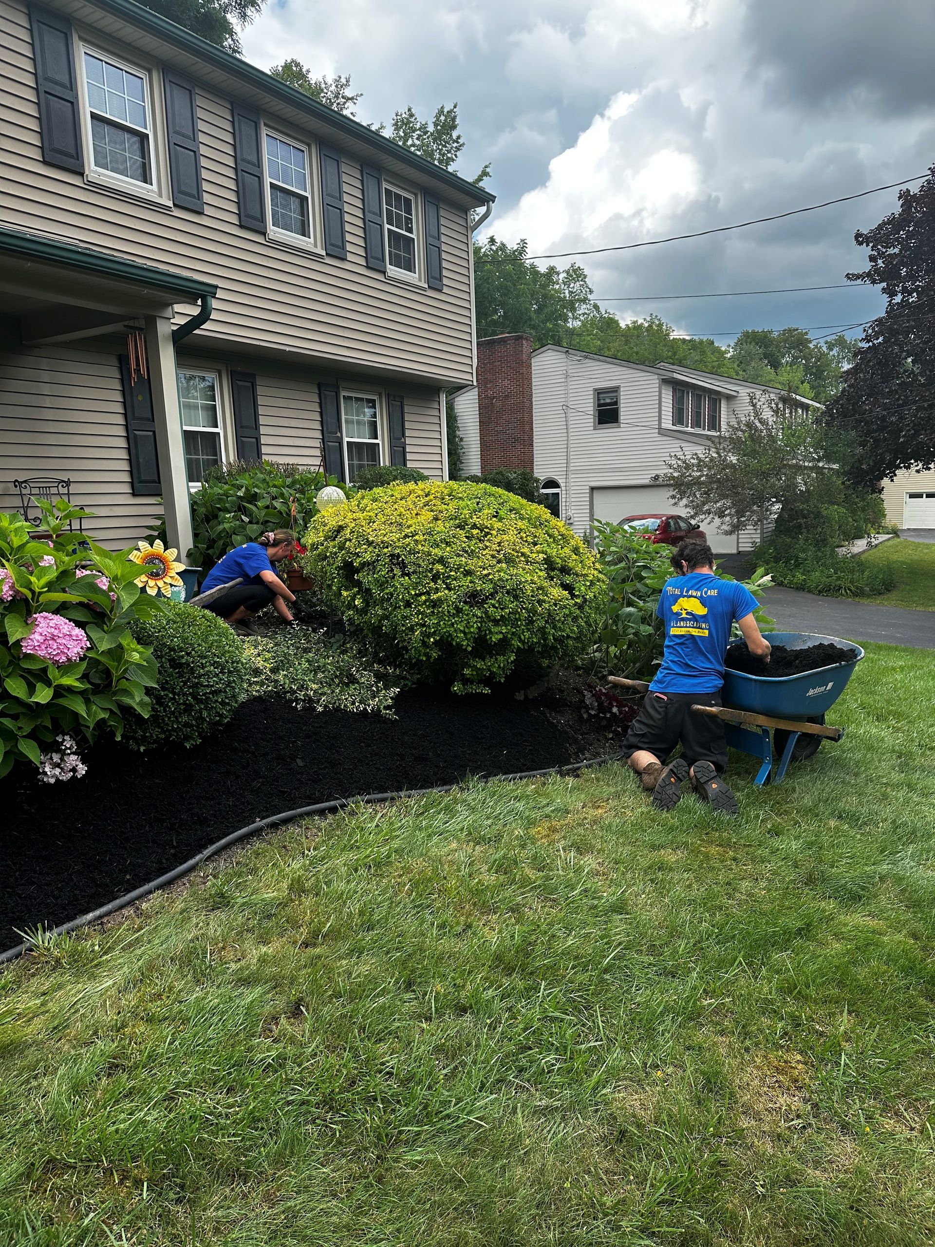 A couple of people are working in a garden in front of a house.
