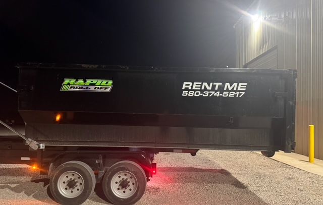 A green dumpster is parked next to an orange trailer