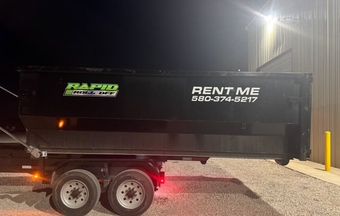 A green dumpster is sitting on the side of the road