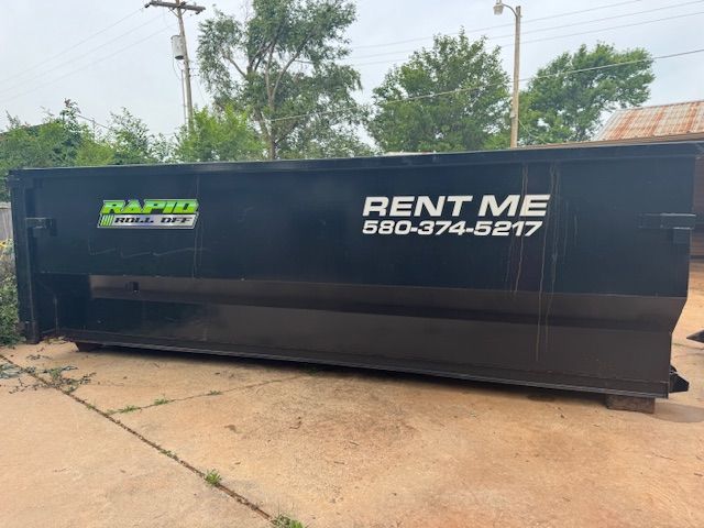 A green dumpster is sitting in front of a brick building