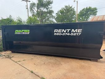 A green dumpster is sitting on the side of the road