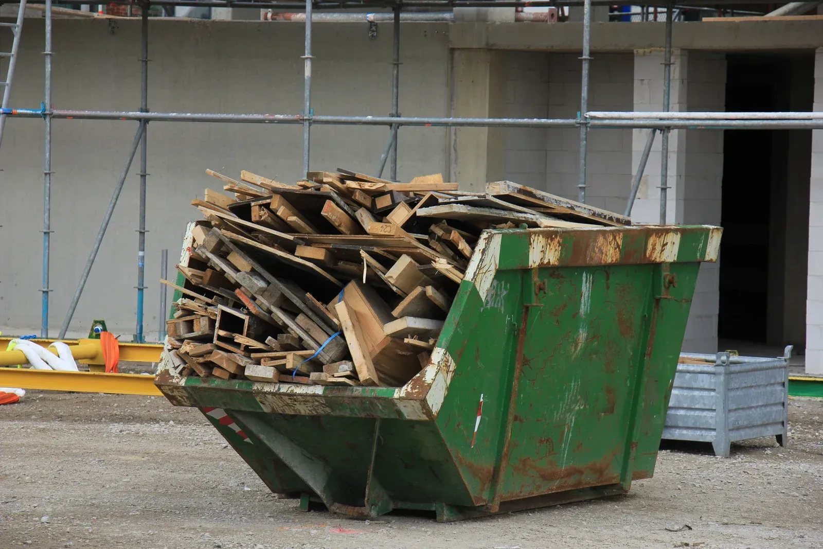 A green dumpster filled with wood is on a construction site.