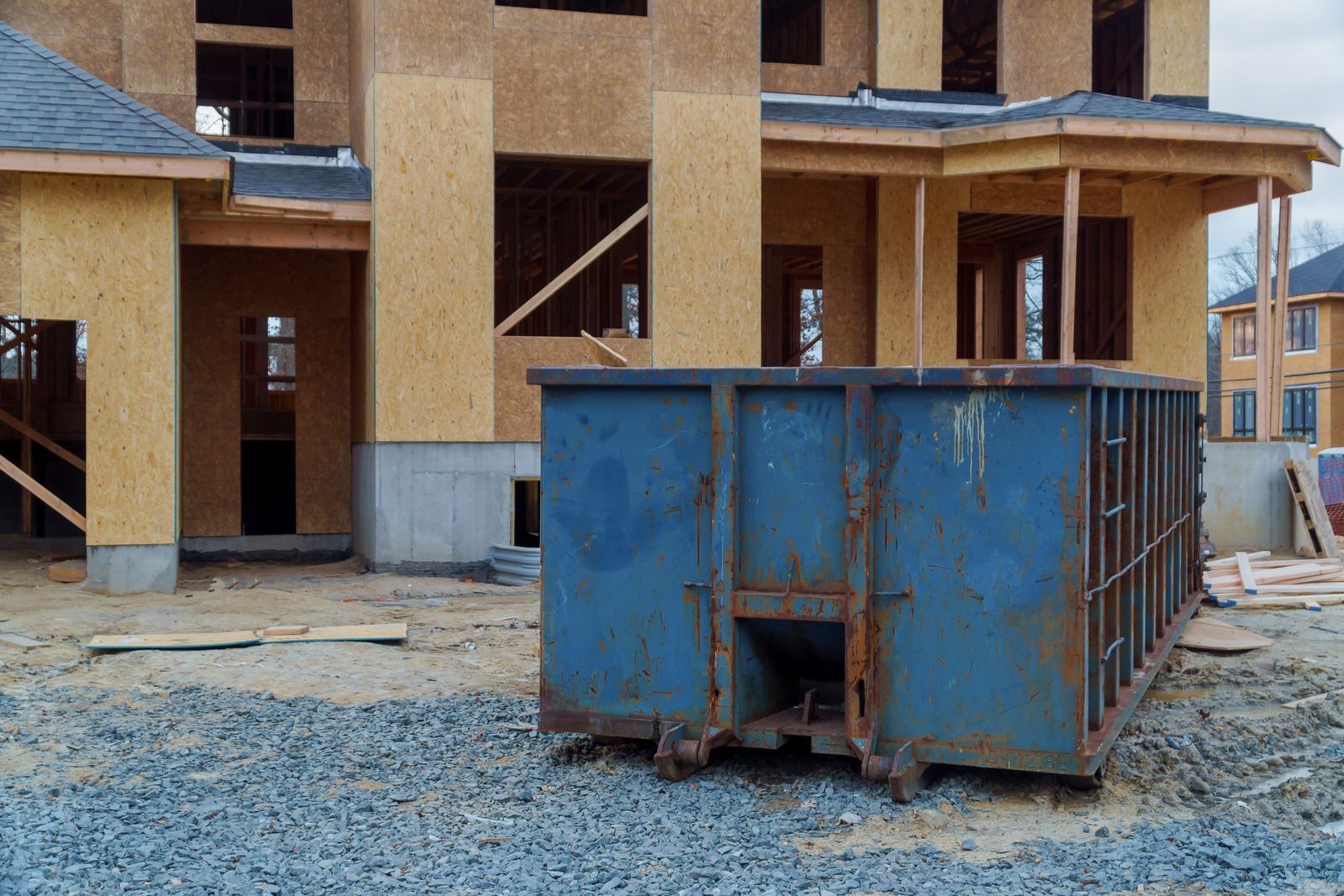 A blue dumpster is sitting in front of a house under construction.