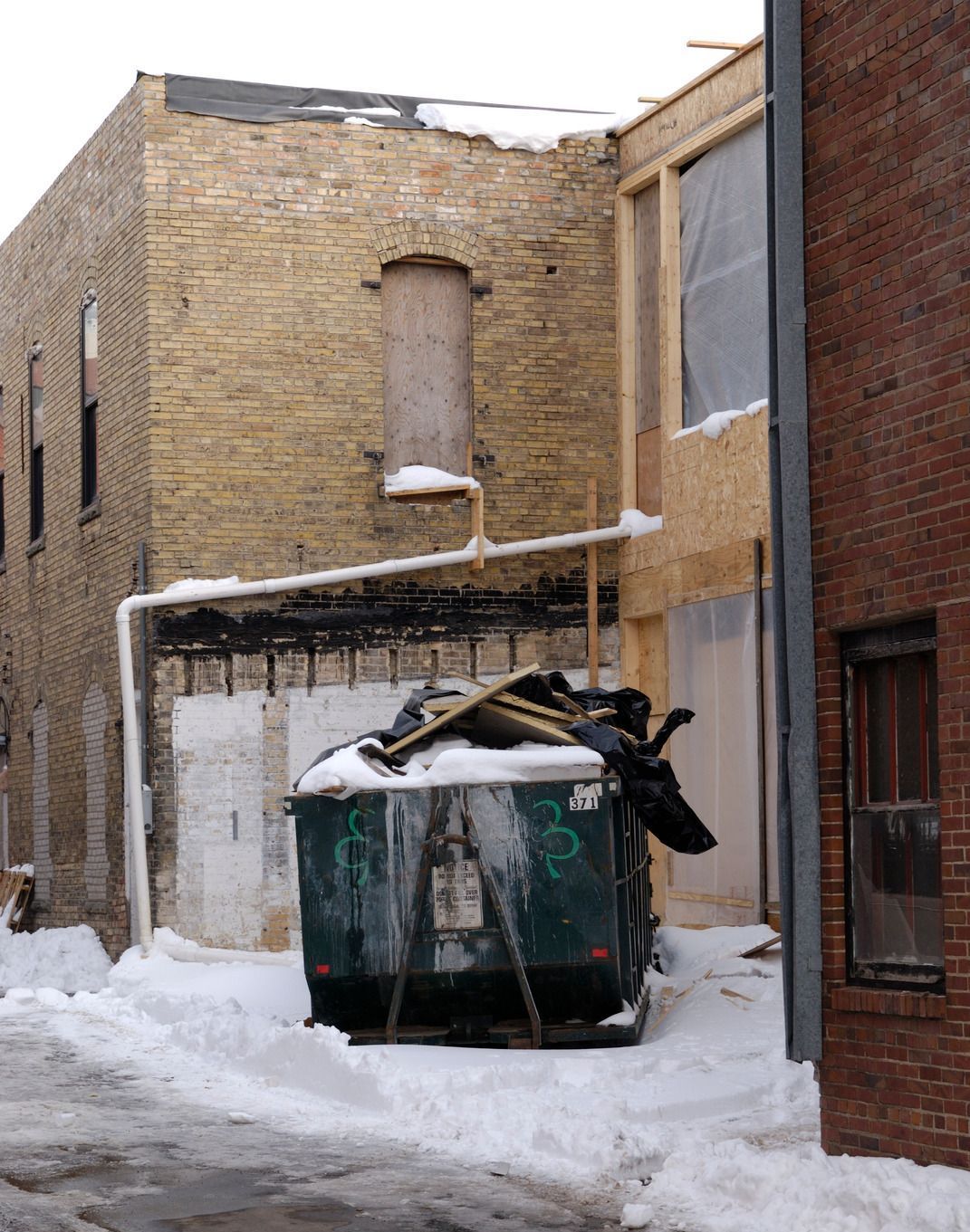 A dumpster is sitting in a snowy alleyway between two brick buildings