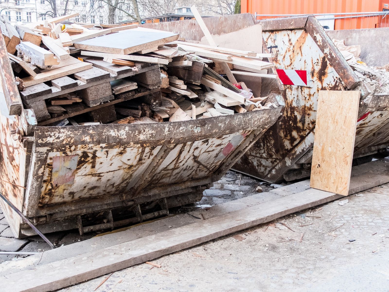 A dumpster filled with wood is sitting on the side of the road.