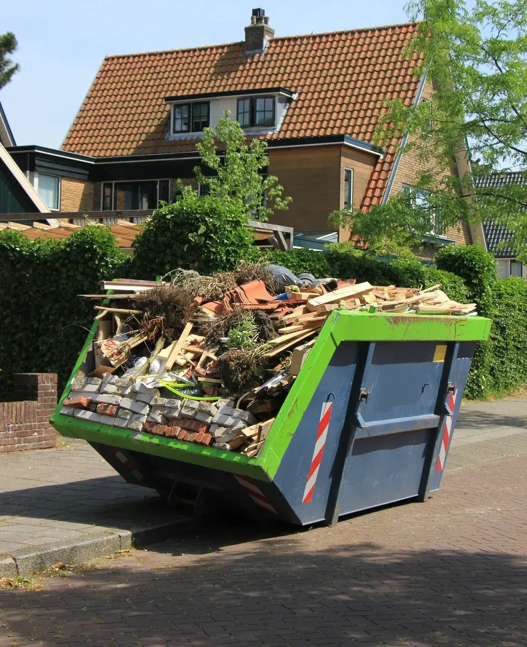 A dumpster filled with garbage is parked in front of a house