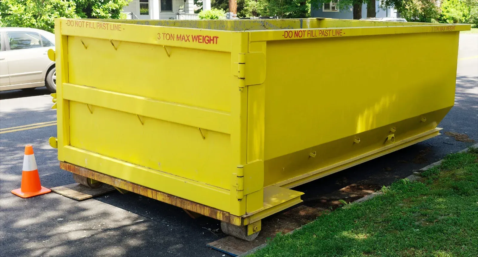 A yellow dumpster is parked on the side of the road next to a traffic cone.