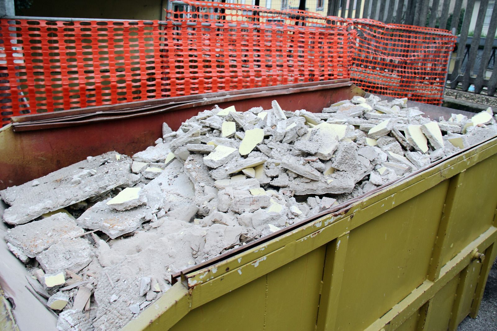 A dumpster filled with concrete and a fence in the background.