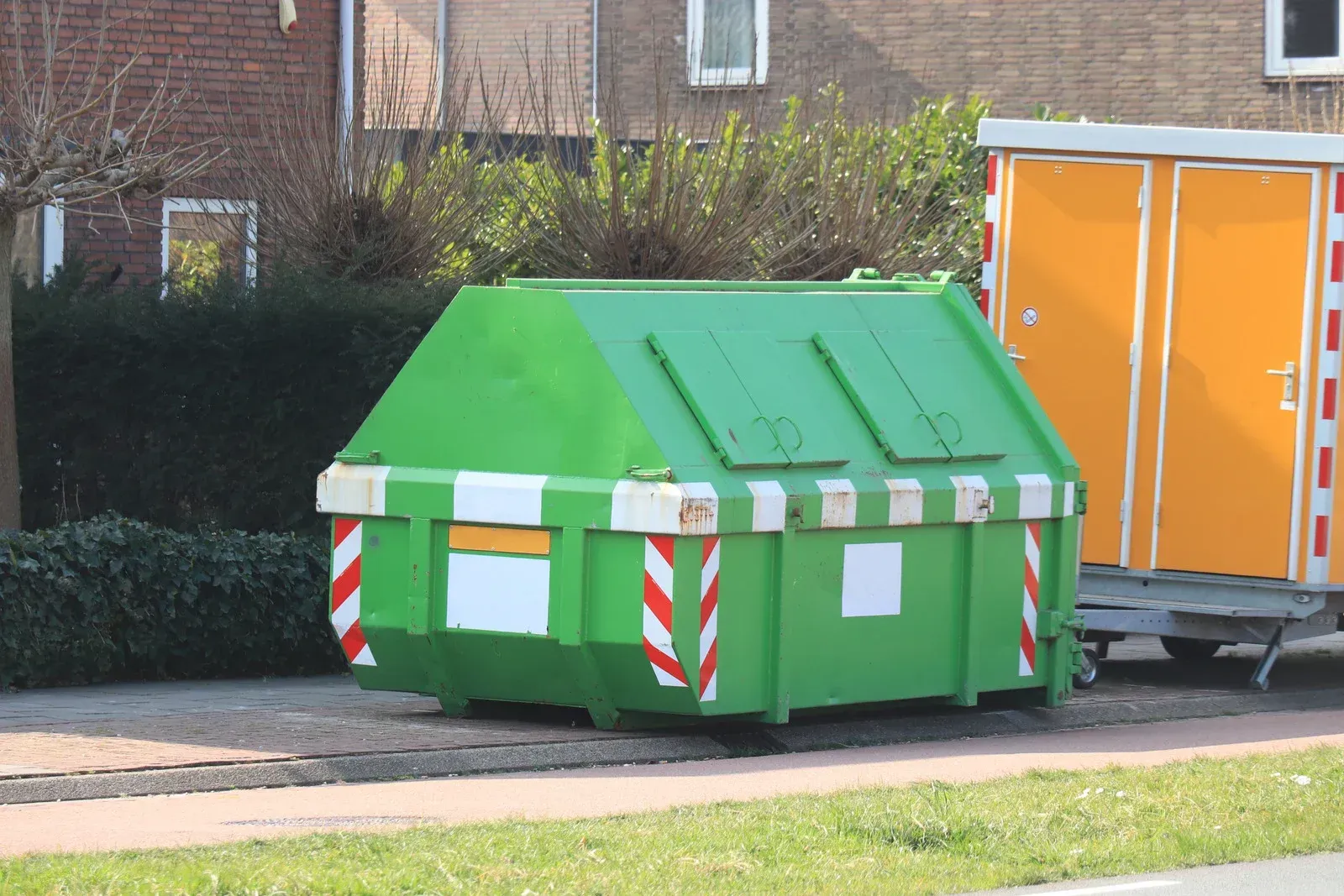 A green dumpster is parked next to an orange trailer