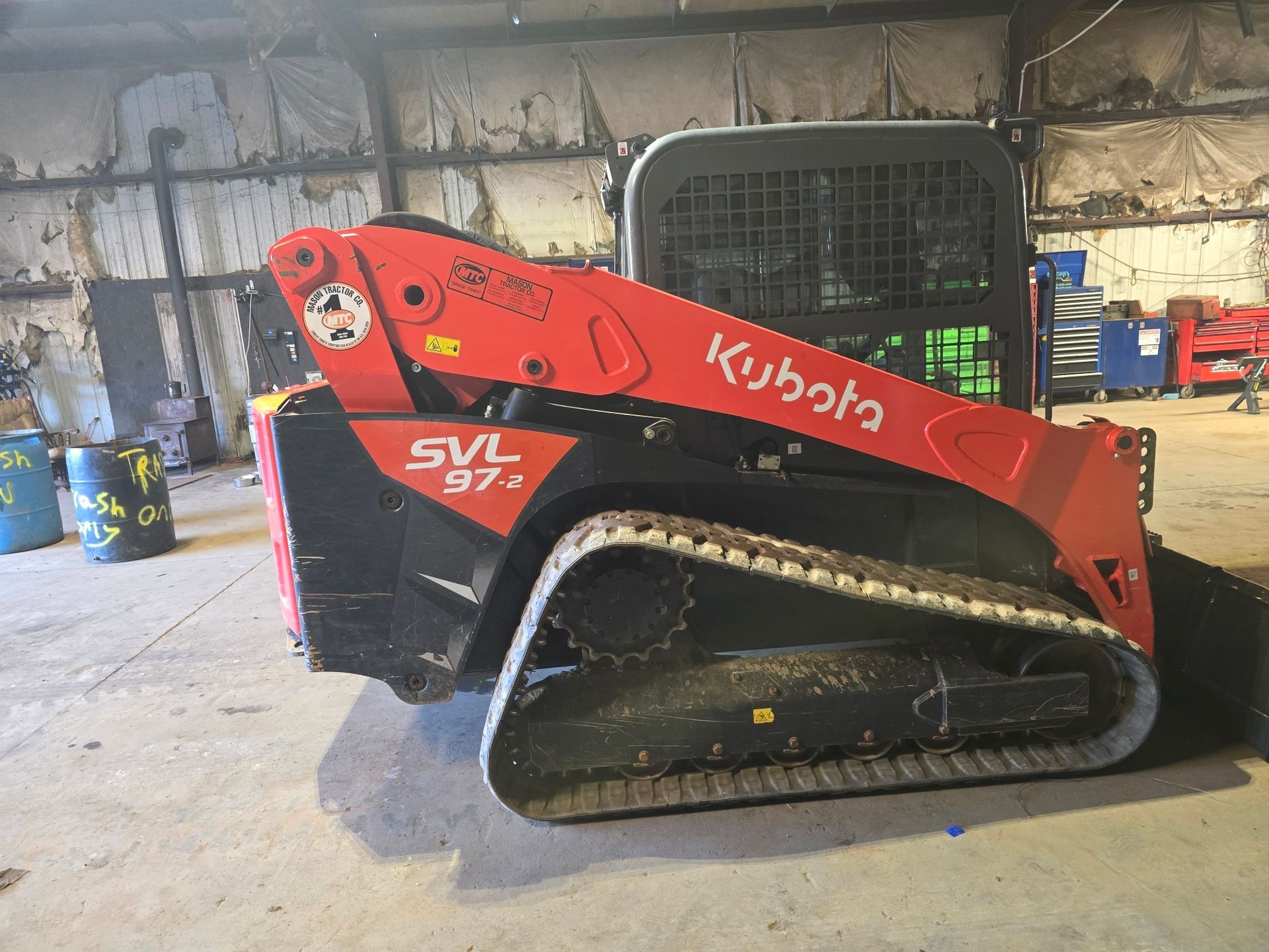 A side profile of an orange and black Kubota SVL 97-2 track loader parked inside a workshop.