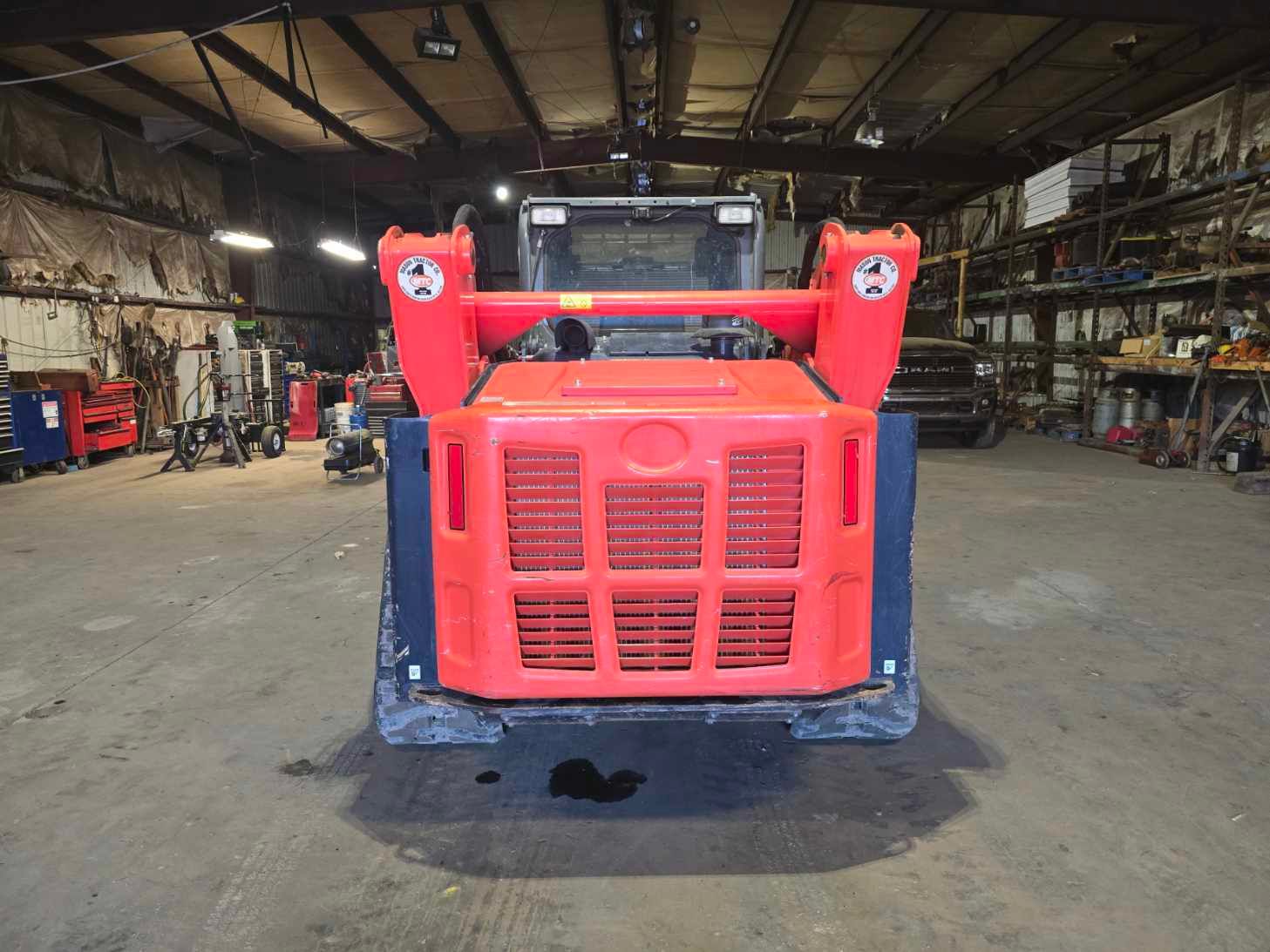 A bright orange skid steer loader parked in the center of a spacious, dimly lit workshop.