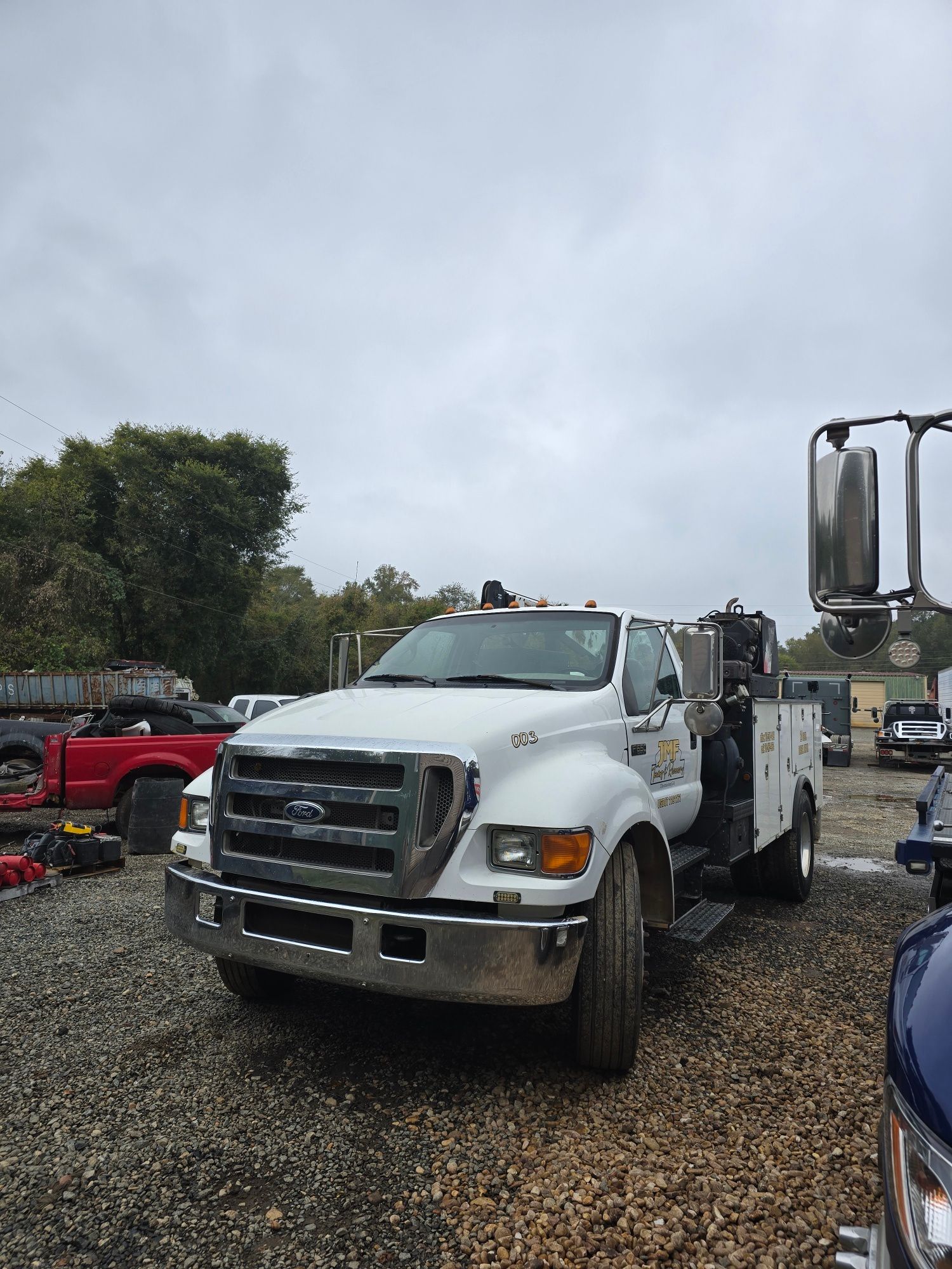 A white Ford service truck parked on a gravel lot under a cloudy sky.