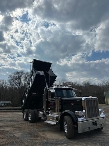 A black dump truck with its bed raised, parked on a gravel lot under a cloudy sky.
