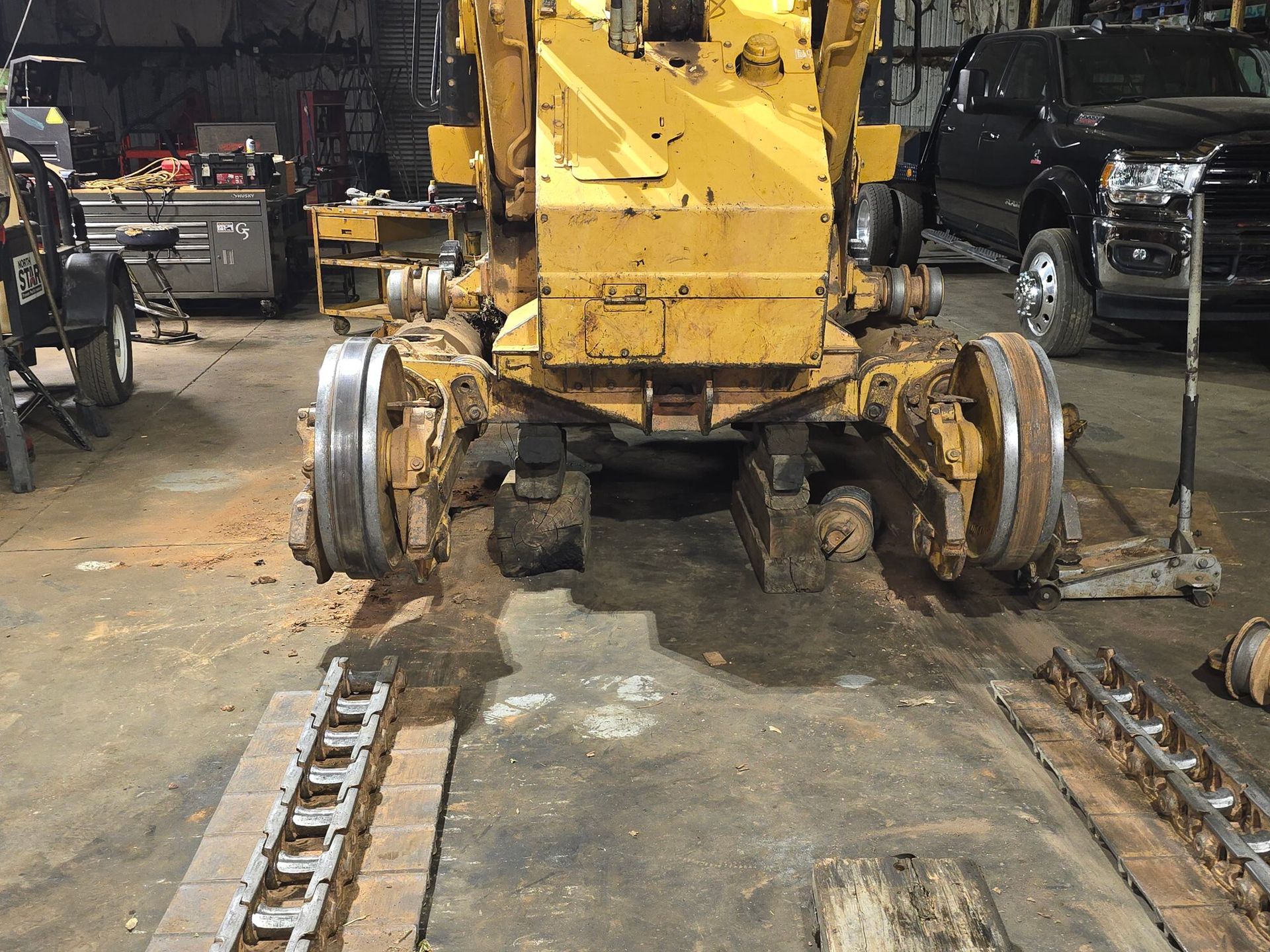 A yellow tracked construction vehicle under maintenance with tracks removed in an indoor workshop.
