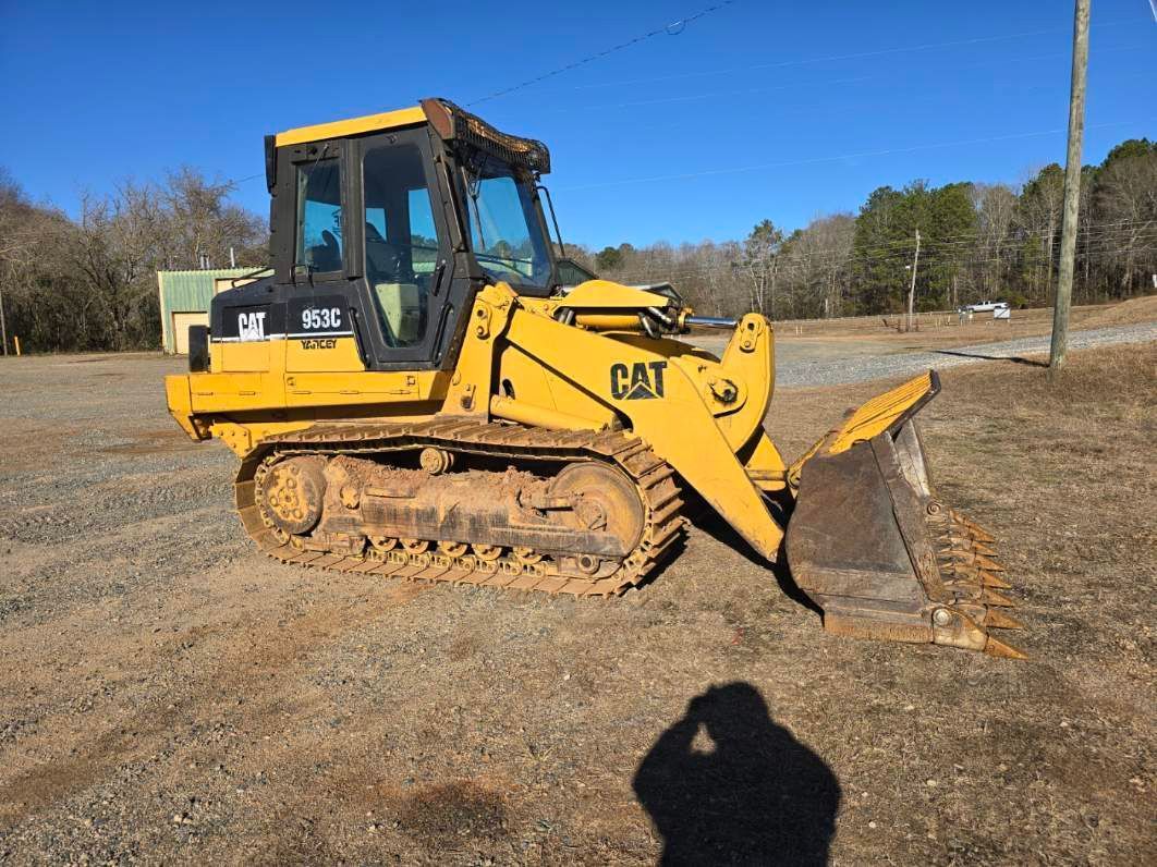 A yellow Caterpillar track loader sits on a dirt field under a clear blue sky.