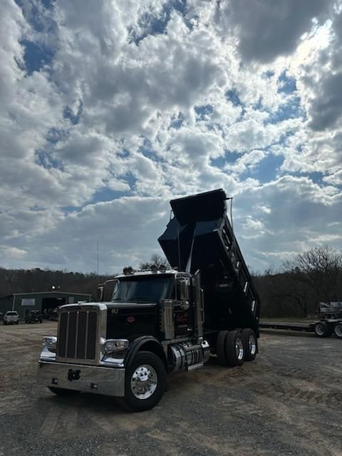 A black dump truck with its bed raised, parked on a gravel lot under a cloudy sky.