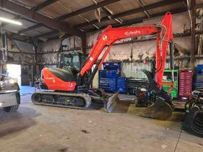 An orange Kubota excavator parked inside a warehouse or garage with tool storage units in the background.