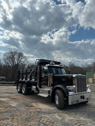 A black Peterbilt dump truck parked on a gravel lot under a cloudy sky.