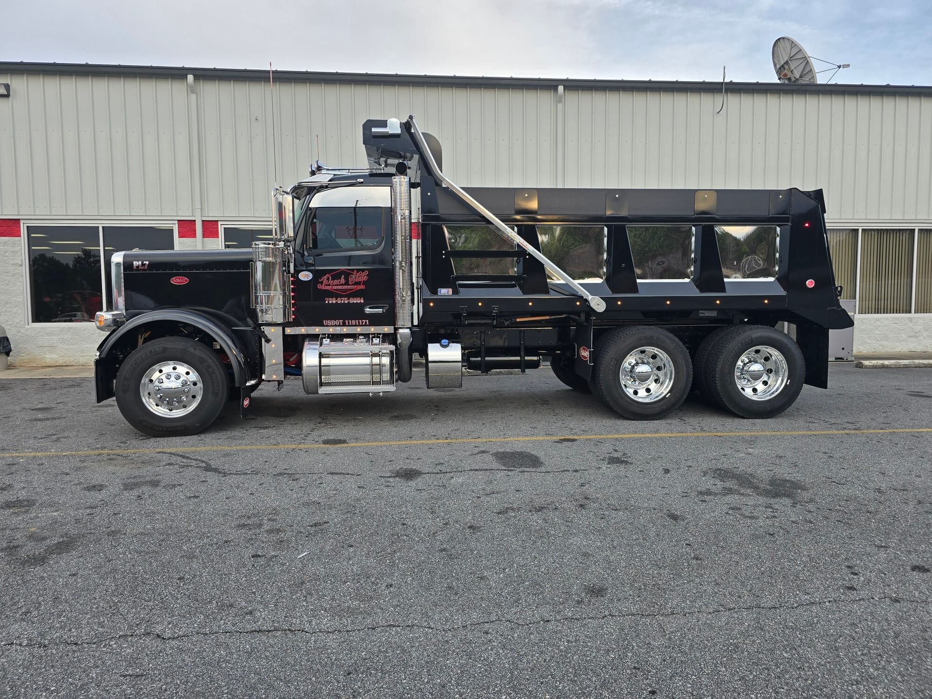 A black dump truck parked in a gravel lot in front of a white warehouse building.