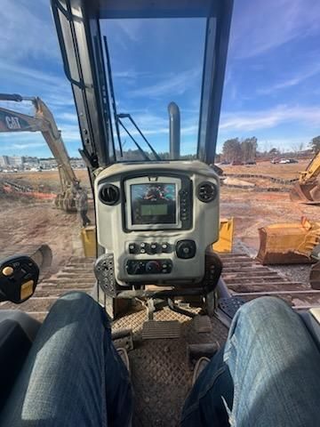 A view from inside the cab of a heavy construction vehicle looking out onto a dirt work site with other machinery.