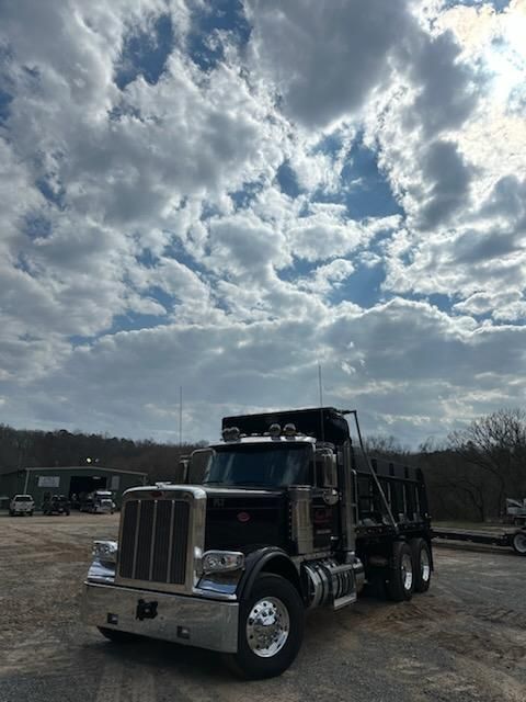 A black Peterbilt semi-truck with a chrome bumper parked in a gravel lot under a dramatic, cloudy sky.