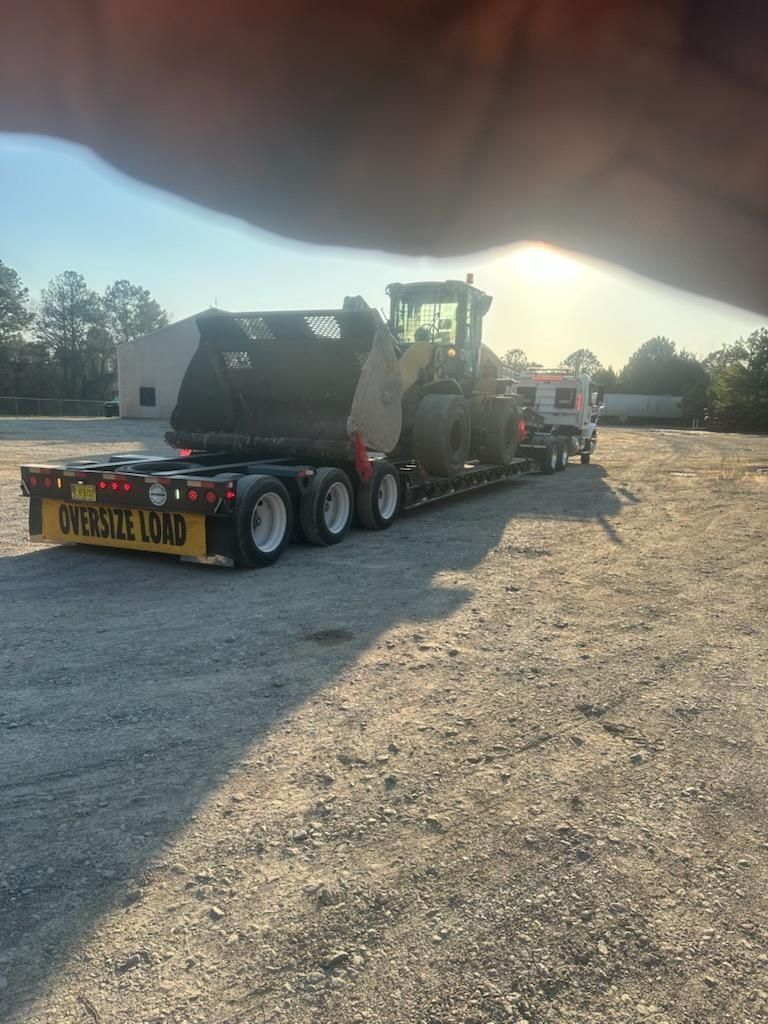 A yellow front loader loaded onto a flatbed trailer parked on a gravel lot during sunset.