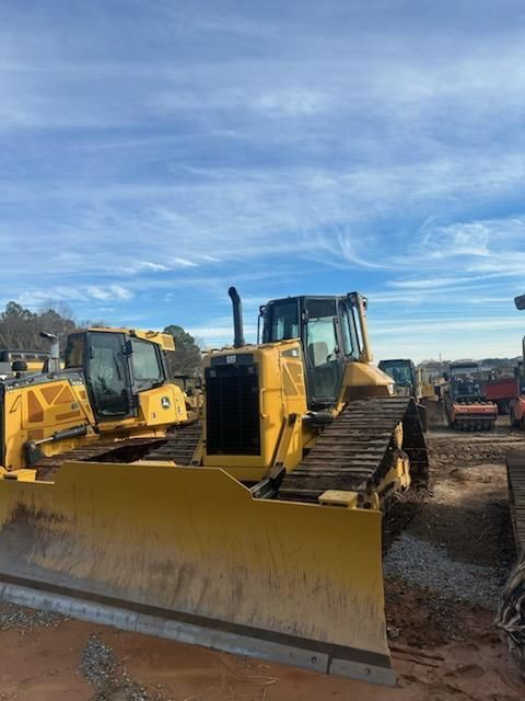 Two yellow construction bulldozers parked side-by-side on a dirt lot under a bright blue sky.