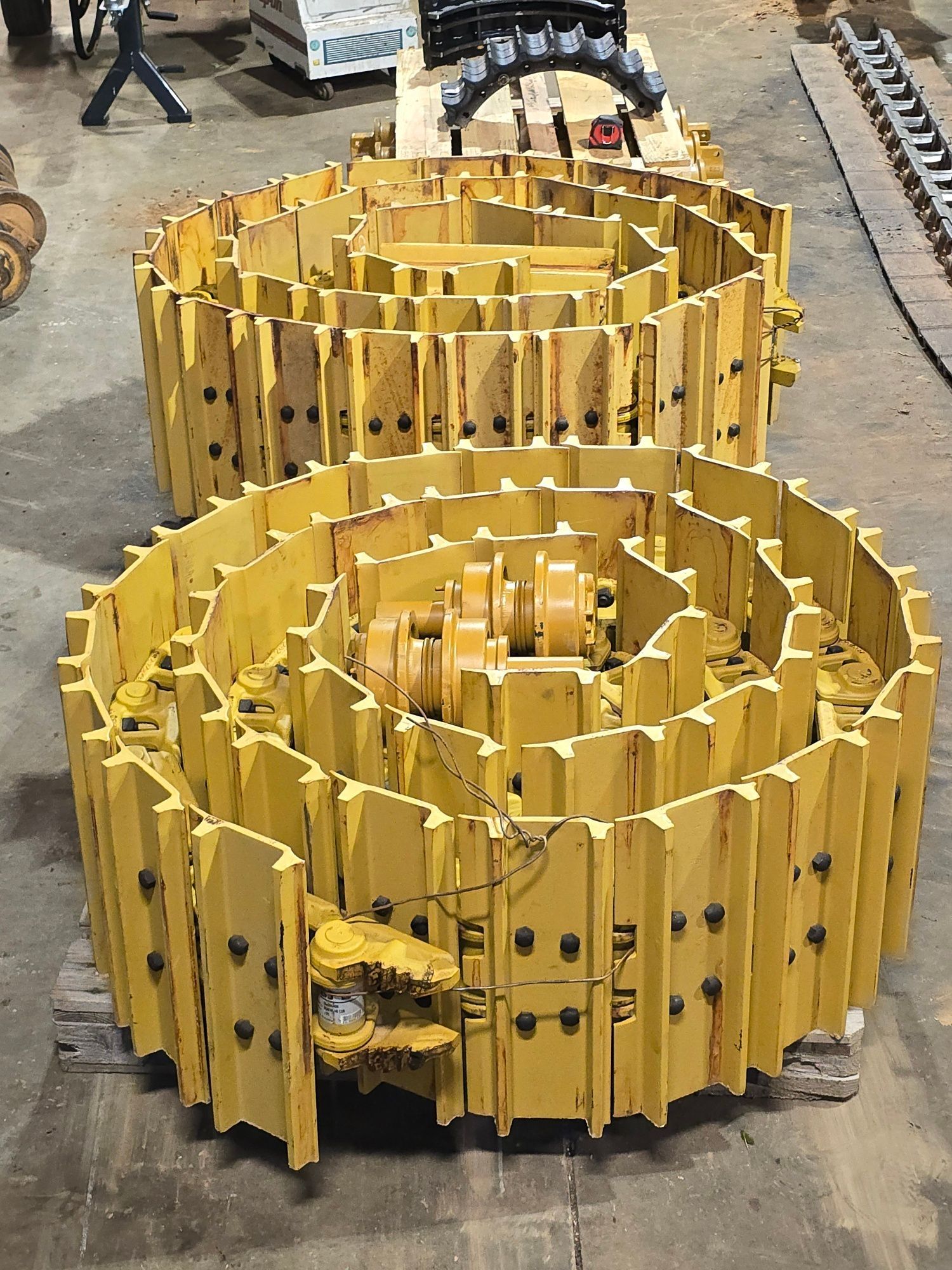 Two coiled yellow bulldozer track assemblies sit on a concrete workshop floor.