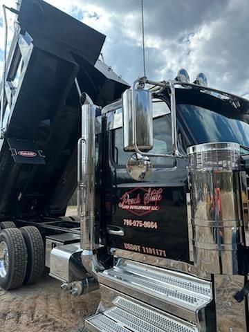 Black dump truck with a raised bed and polished chrome details parked outdoors under a cloudy sky.