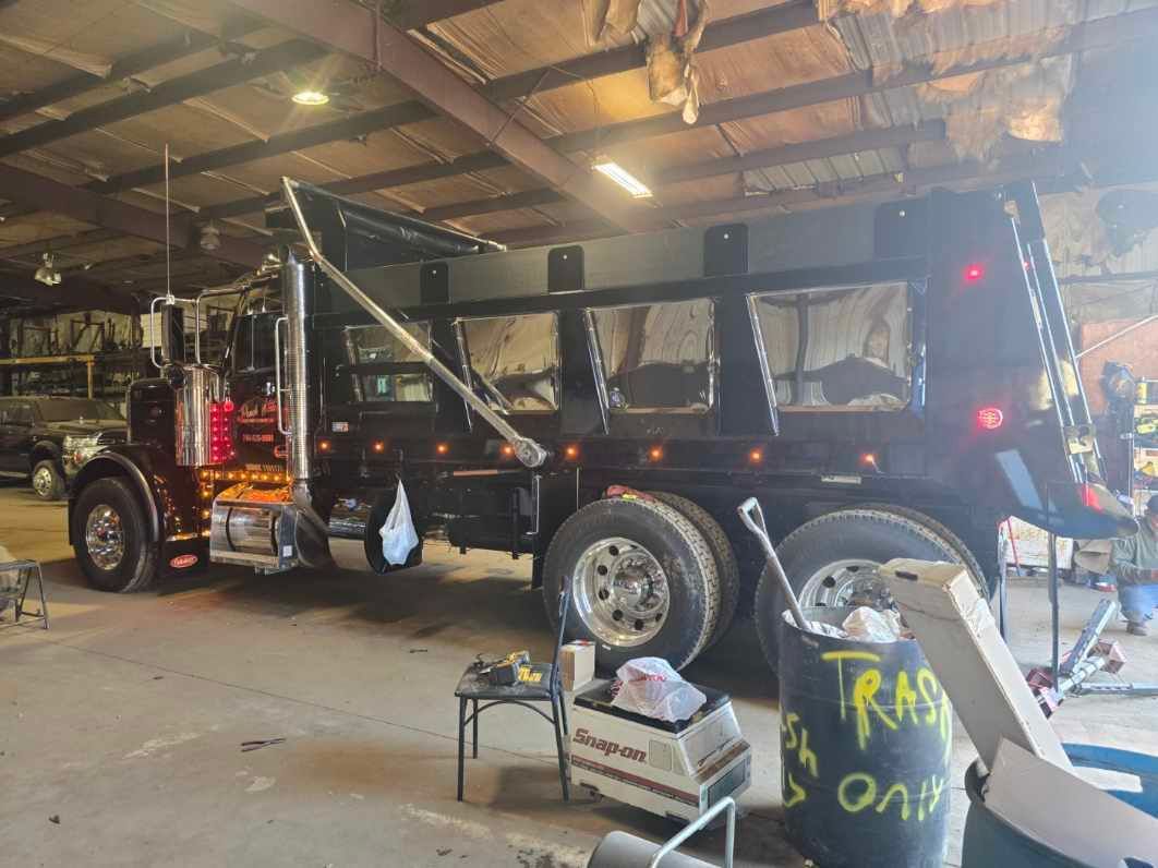 A shiny black dump truck parked inside a workshop with a trash bin in the foreground.