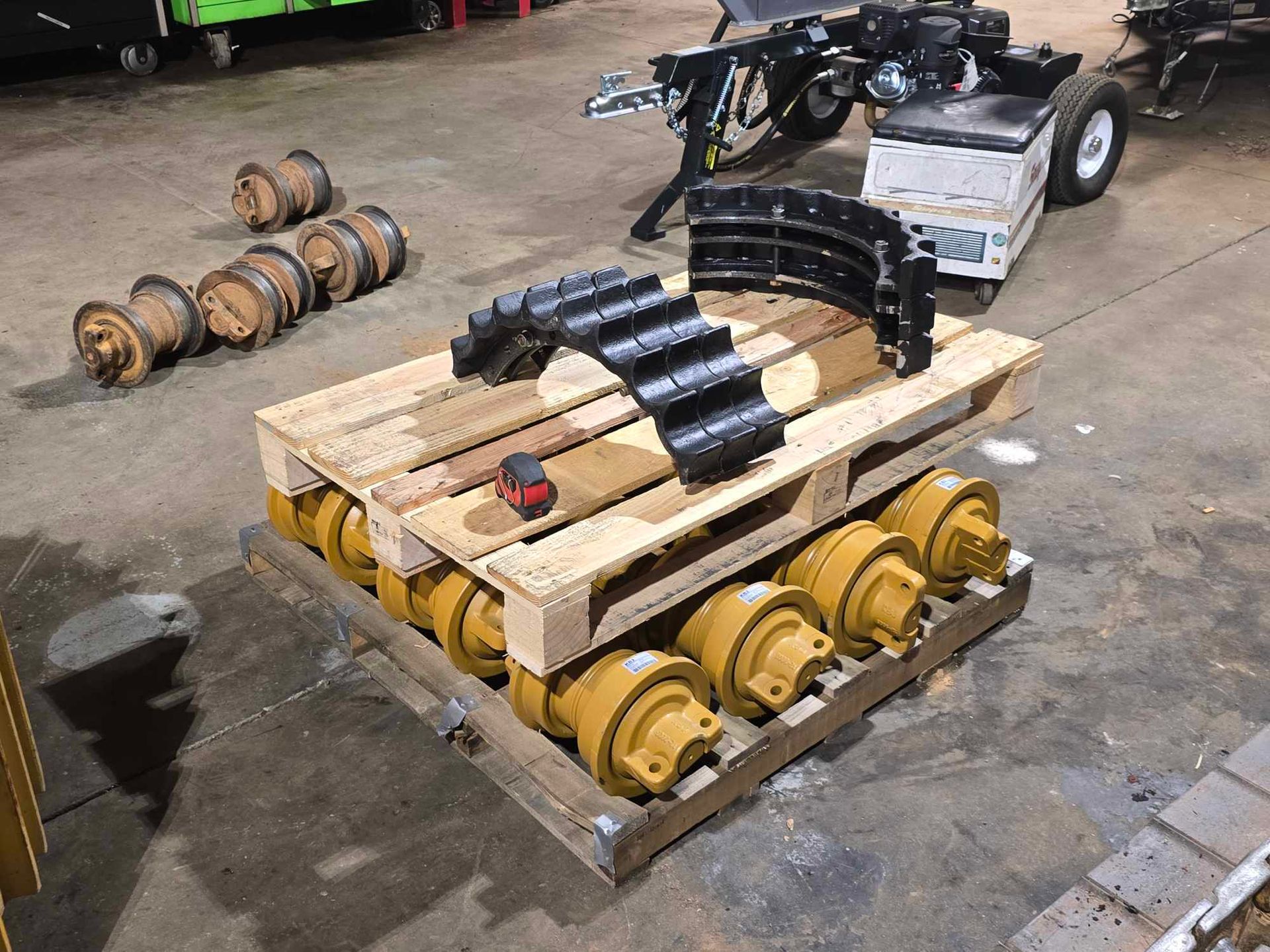 A wooden pallet holds heavy yellow rollers and curved black track parts in a workshop, with loose rollers on the floor.