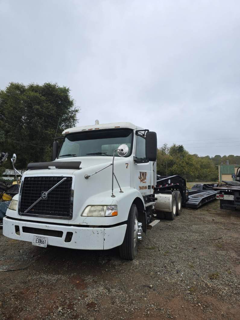 A white Volvo semi-truck parked on a gravel lot under a cloudy sky.