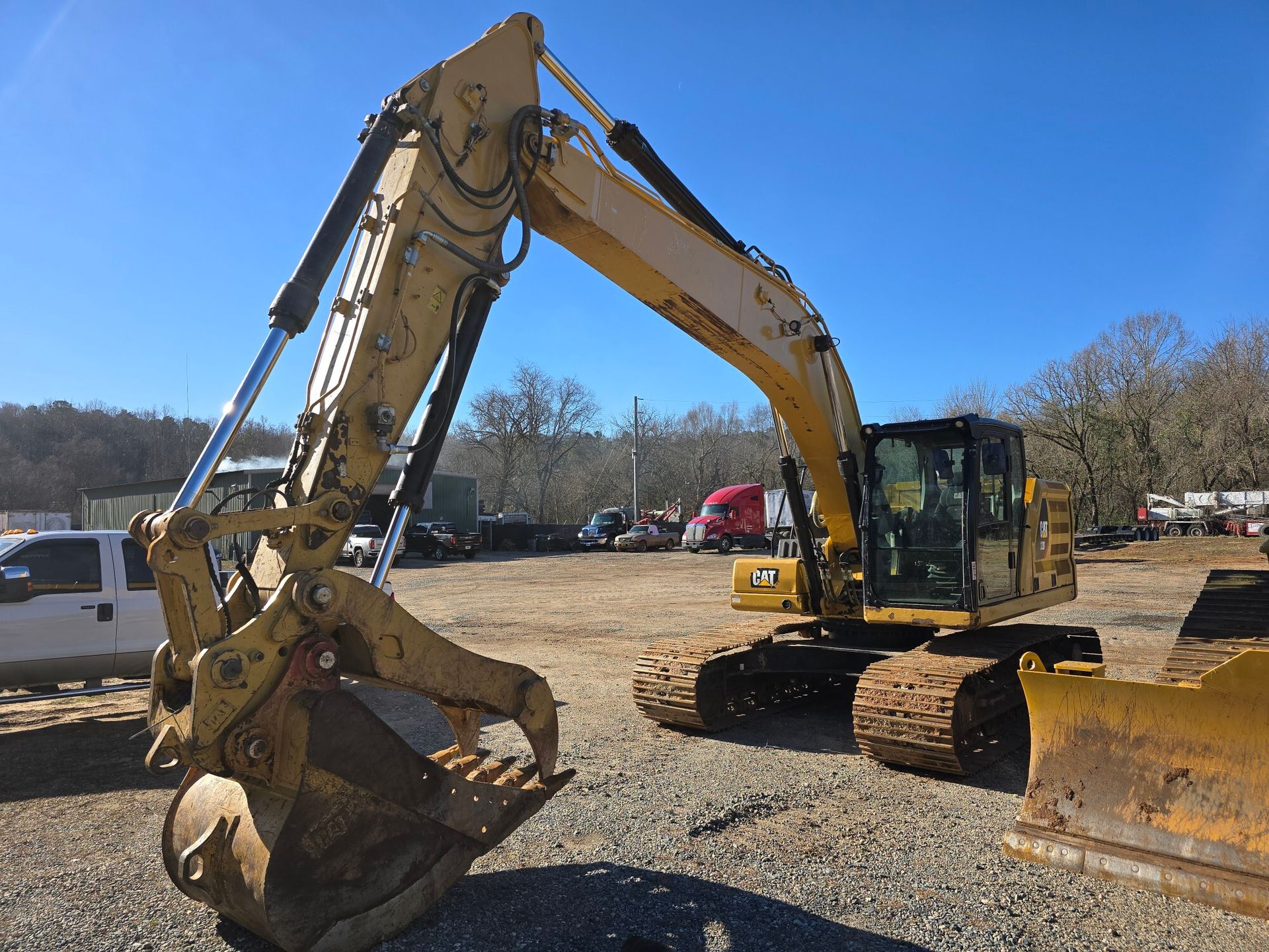 A yellow Caterpillar excavator sits parked on a gravel lot under a clear blue sky.