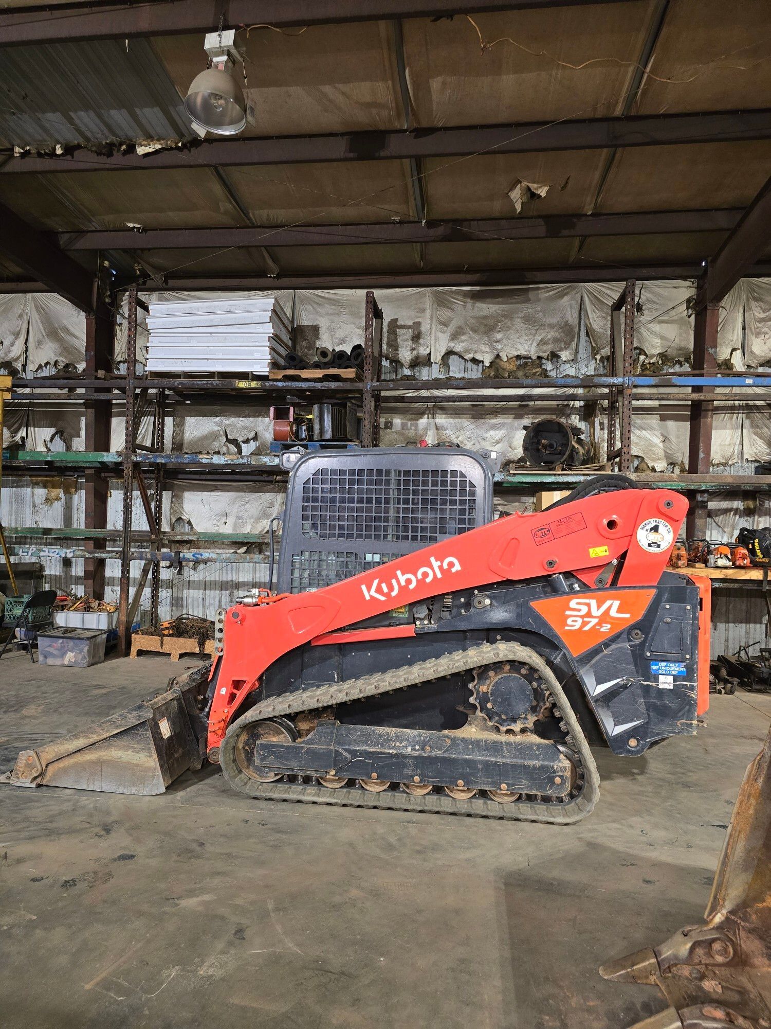 A bright orange and black Kubota SVL 97-2 track loader parked inside a dimly lit workshop.
