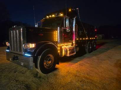 A black Peterbilt dump truck with bright amber cab and running lights parked outdoors at night.