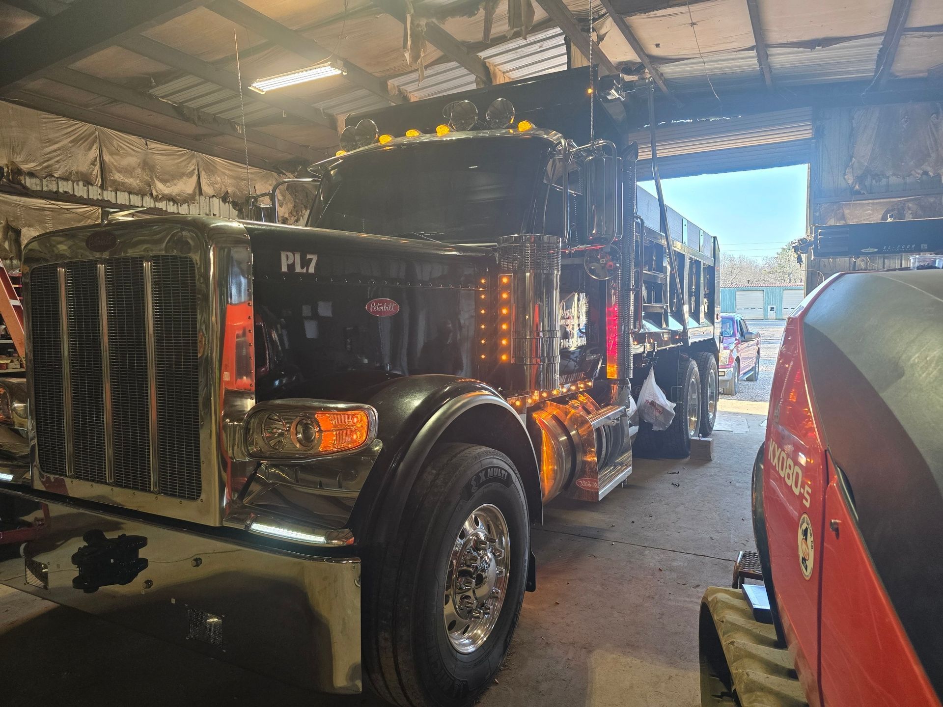 A polished black Peterbilt dump truck with chrome accents parked inside a dimly lit workshop.