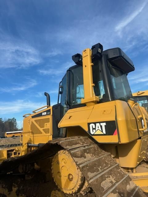 A yellow Caterpillar bulldozer parked outdoors against a blue sky with visible clouds.