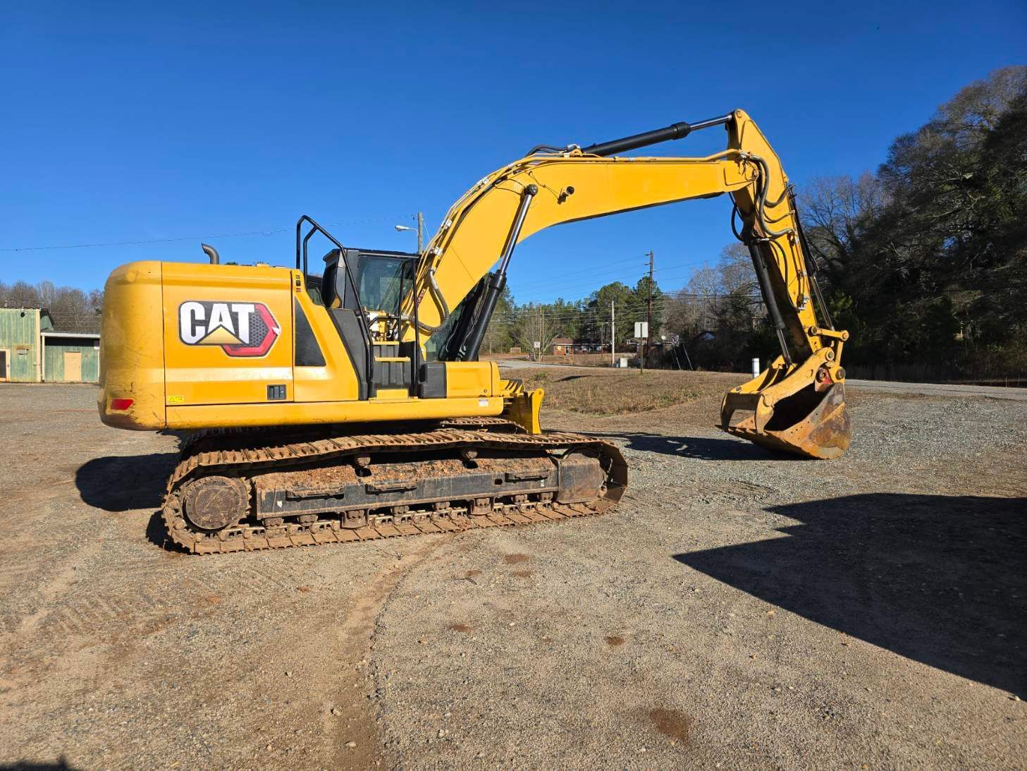 A yellow Caterpillar excavator parked on a gravel lot under a clear blue sky.