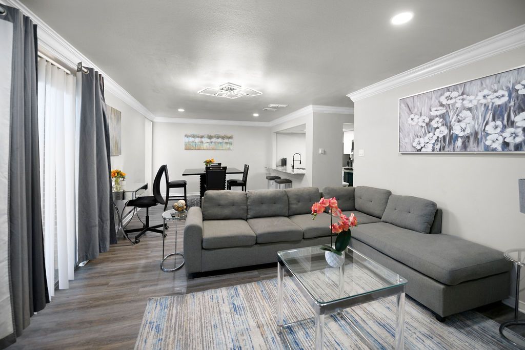 Gray sectional sofa in a light-filled living room with a dining area and kitchen visible in the background.
