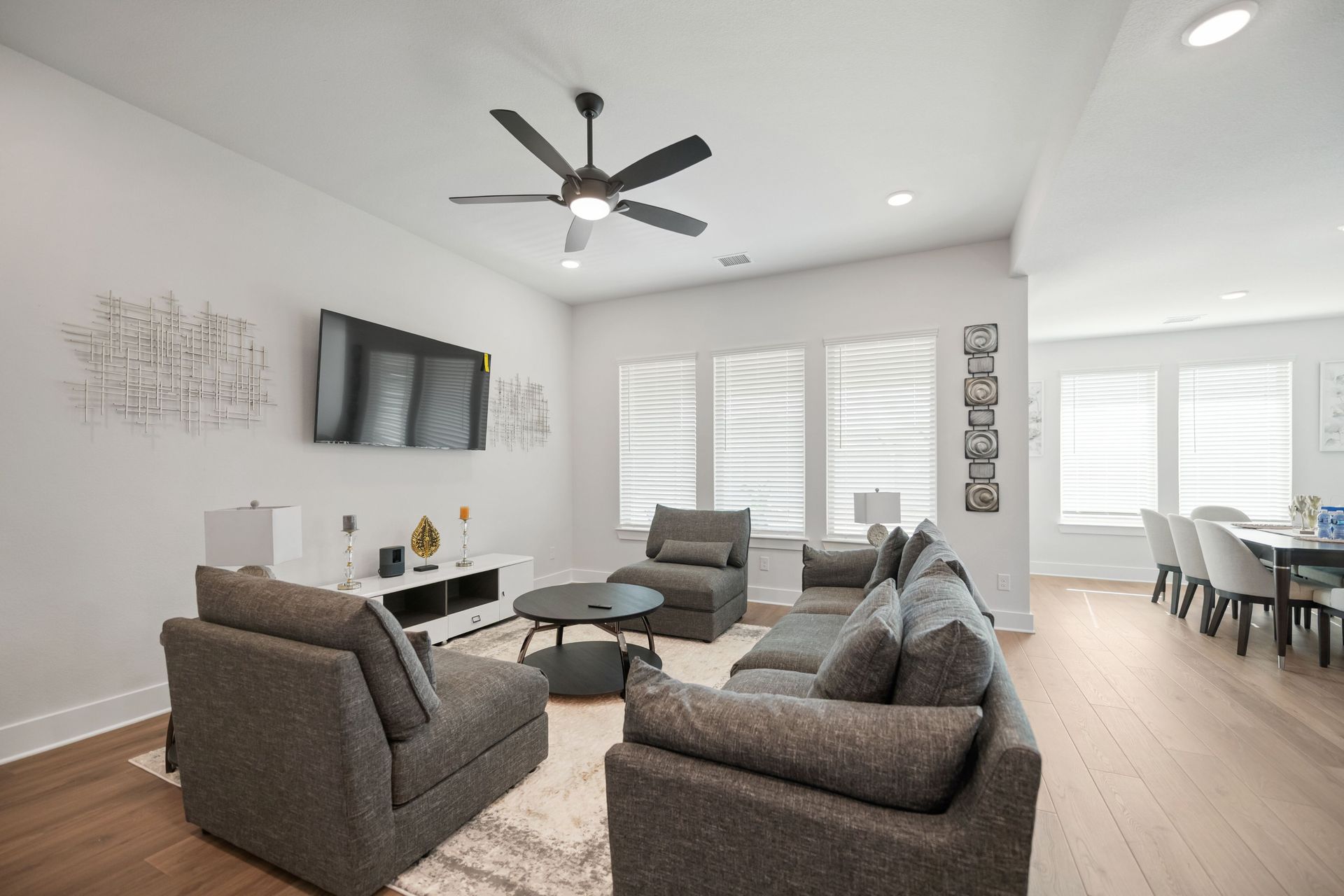 Bedroom with bed, dresser, TV, and sliding doors to balcony. White walls, gray wood floor.