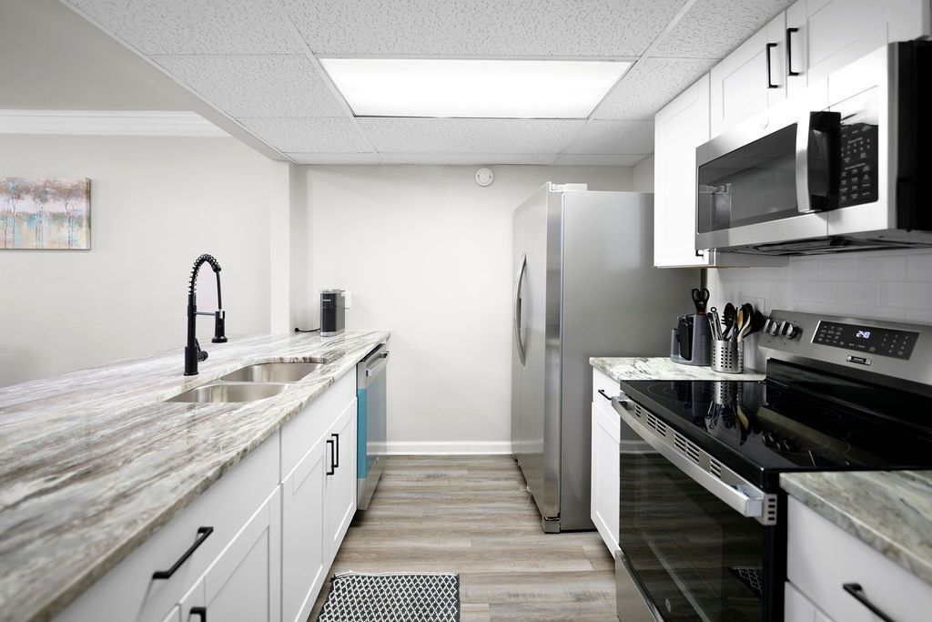 Modern kitchen with white cabinets, stainless steel appliances, and a long countertop with a sink.