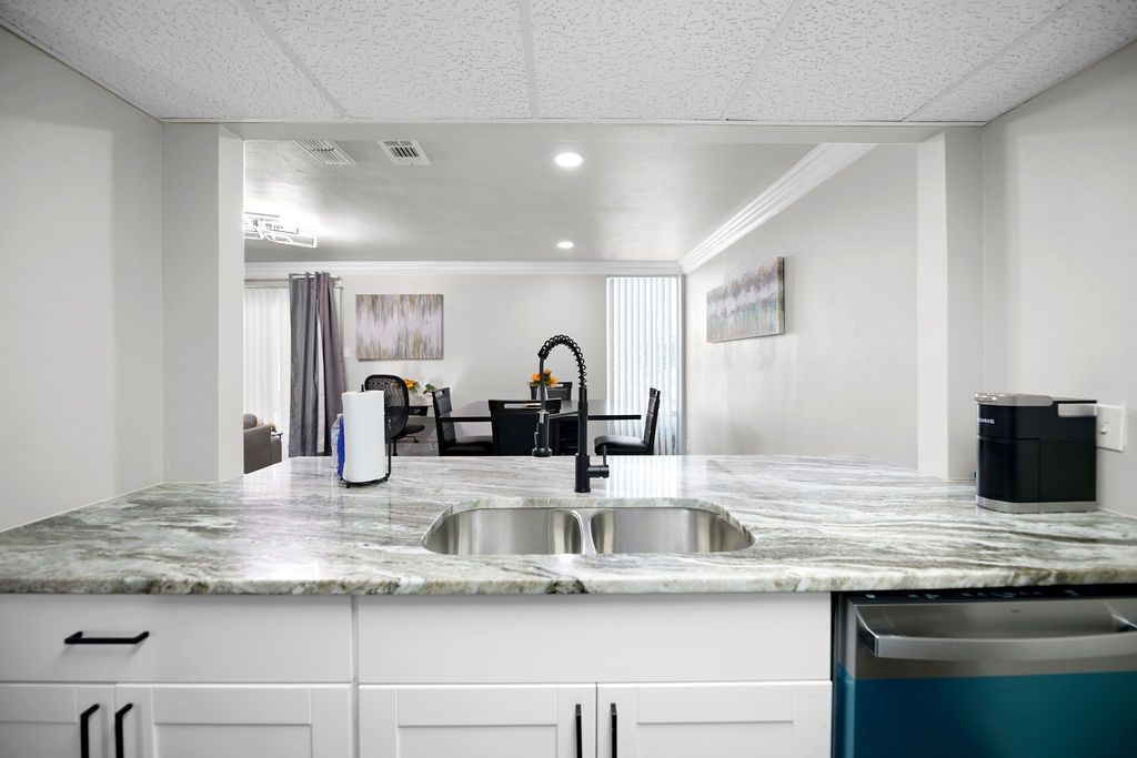 Kitchen with a granite countertop, stainless steel sink and faucet. A pass-through to the dining area is visible in the background.