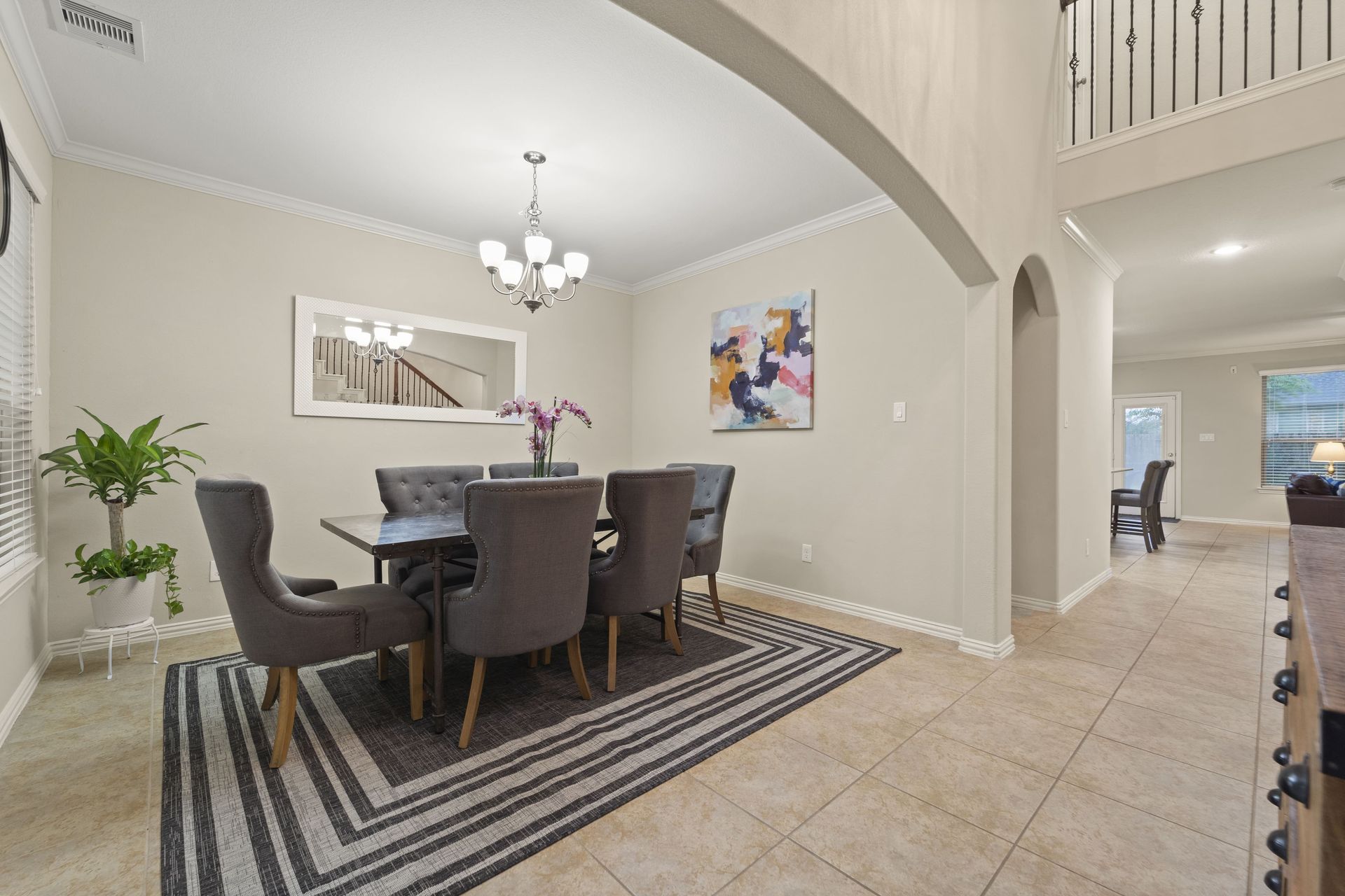 Formal dining room with a dark rectangular table and six gray upholstered chairs, a rug with dark and light stripes, and art on the wall.
