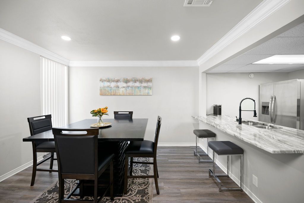 A dining room with a dark table and chairs, adjacent to a kitchen with a bar and stools.