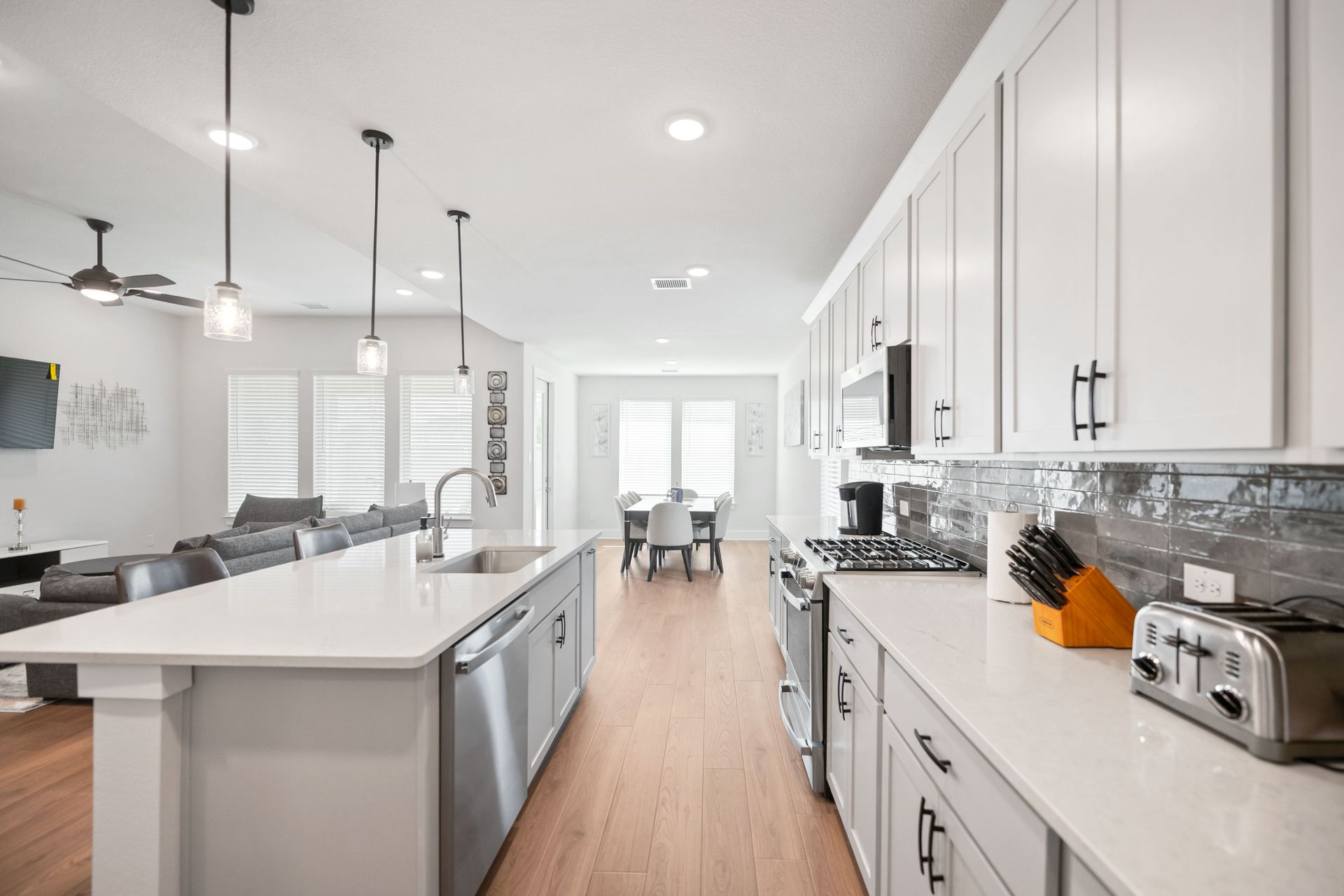 Modern kitchen with white cabinets, stainless steel appliances, and island. Open to living and dining areas.