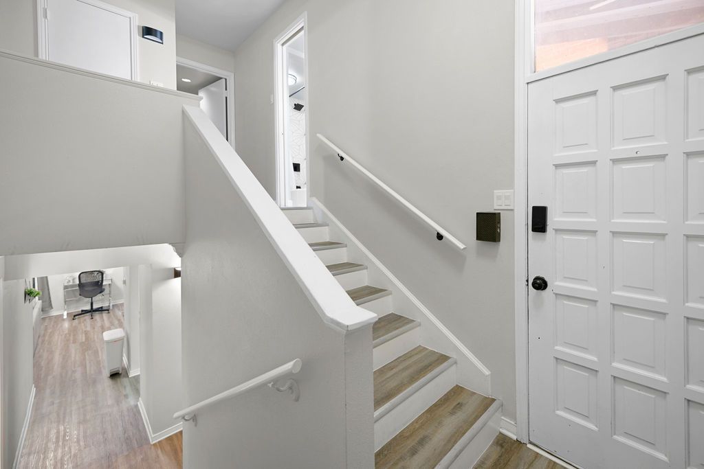 A white interior staircase leads to an upper level, with a doorway and door on the right. A hallway is visible below on the left.